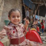 A cheerful young girl smiles while swinging outdoors in Idlib, Syria, capturing the innocence of childhood.