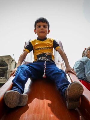 A group of children enjoy playing on a slide in Idlib, capturing joy amidst urban surroundings.