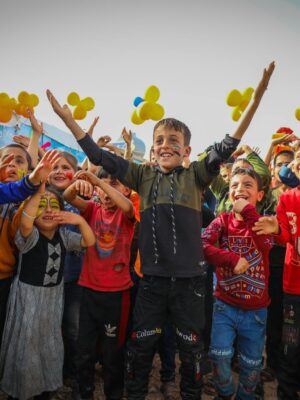 A vibrant group of children celebrate together outdoors in Idlib, Syria.