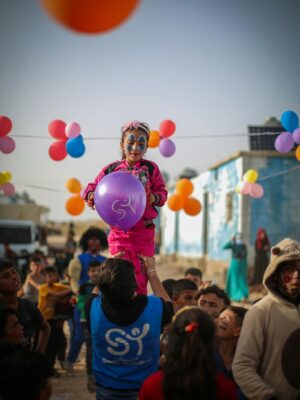 Vibrant festival scene with children playing and balloons in Idlib, Syria, showcasing joy and community.